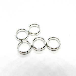 May include: Five shiny silver rings are arranged on a white background. The rings have a smooth, polished surface and a simple, classic design. The rings are round and appear to be made of metal. The image is well-lit, highlighting the reflective quality of the rings.