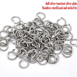 May include: A collection of dull silver tone stainless steel jump rings. The text in the image reads: dull silver tone(not silver plated) Stainless steel(Lead and nickel free). These circular metal connectors feature a small opening.