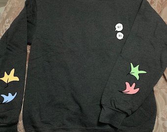 Könnte beinhalten: Ein dunkelgrauer Pullover mit einem weißen "HI"-Motiv auf der Vorderseite und bunten Blattdesigns auf den Ärmeln.