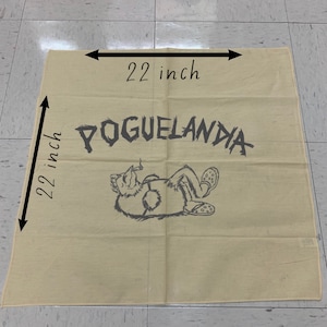 May include: A beige square cloth, 22 inches by 22 inches, with the word "POGUELANDIA" in dark gray, along with a cartoon illustration of a relaxed creature wearing sandals. The cloth is made of a light-colored fabric.