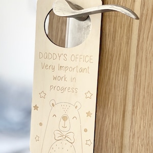 May include: Wooden door hanger with the text "Daddy's Office Very Important Work in Progress" and a cartoon bear with a bow tie. The hanger has a hole at the top for hanging on a door knob.
