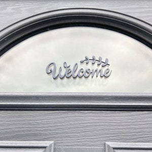 May include: A black welcome sign with a leafy design, attached to a frosted glass door.