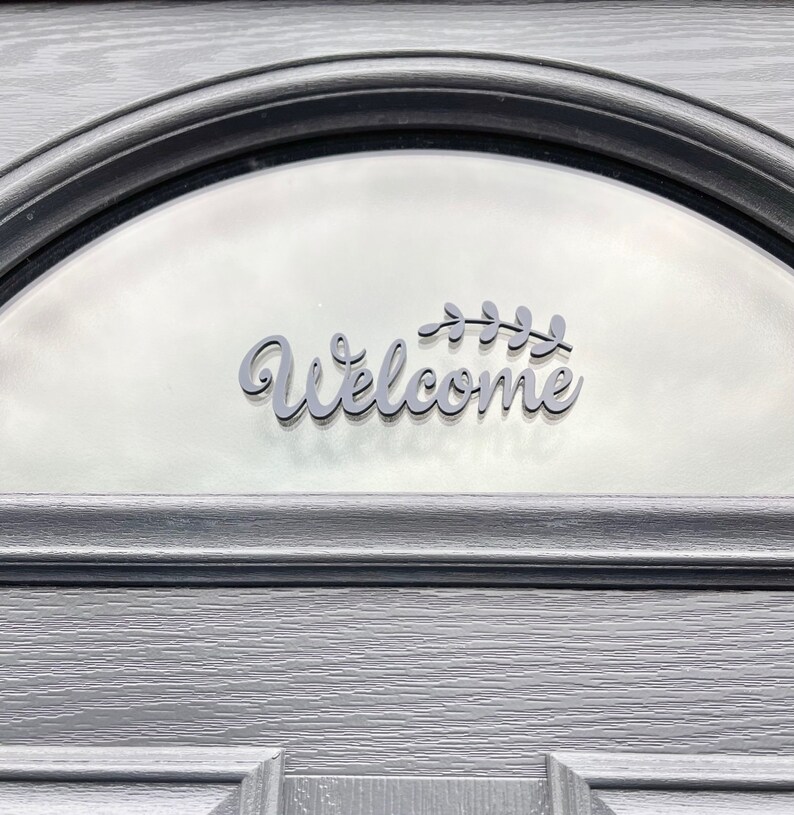 May include: A black welcome sign with a leafy design, attached to a frosted glass door.