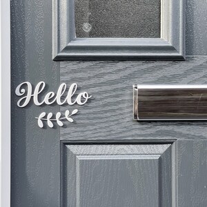 May include: A grey front door with a silver letterbox and a white vinyl sign that says "Hello" with a small leafy branch design.
