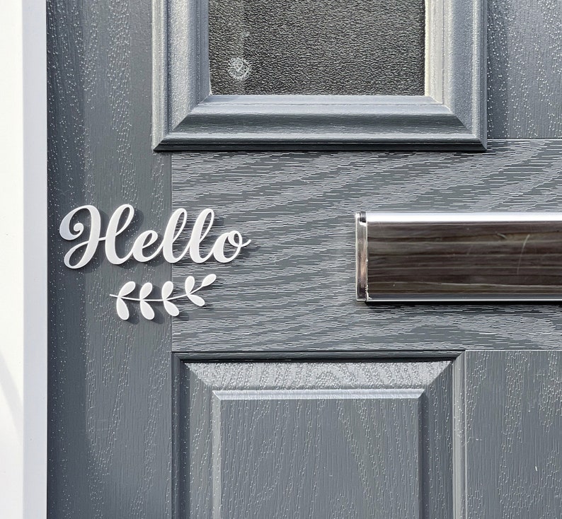 May include: A grey front door with a silver letterbox and a white vinyl sign that says "Hello" with a small leafy branch design.