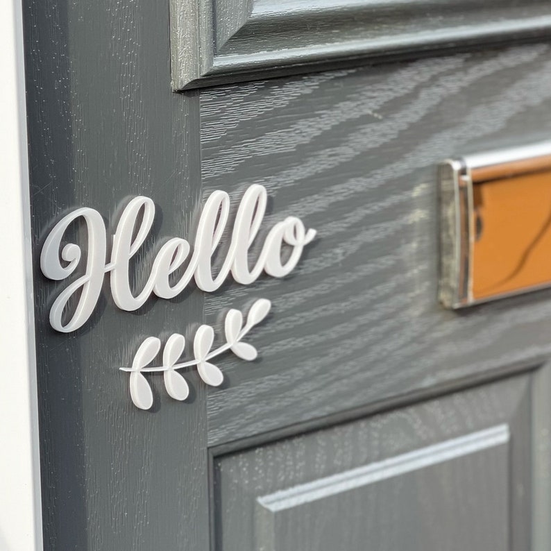 May include: White 3D "Hello" sign with a white leafy branch attached to a grey door.