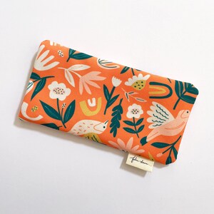 May include: Orange eye mask with a floral and bird print. The fabric has a textured surface. The eye mask has a small label that says "Fable Lane".