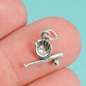 May include: Silver charm featuring a baseball glove catching a ball and a baseball bat. The charm is designed to be attached to a necklace or bracelet.