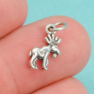 Puede incluir: Un amuleto de plata en forma de alce con un bucle para sujetarlo a un collar o pulsera. El amuleto mide aproximadamente 2,5 cm de alto y es una opción popular para los amantes de la naturaleza.