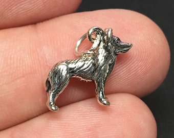 May include: Silver charm of a standing wolf, the wolf is facing to the right, the charm is shown in the hand of a person.