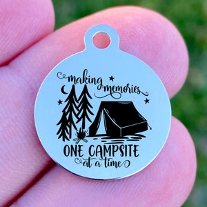 Op de afbeelding: Een ronde, zilverkleurige bedel met een campingthema. De bedel heeft een zwarte illustratie van een tent, bomen en een kampvuur, met de tekst "making memories ONE CAMPSITE at a time."