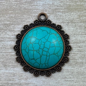 May include: A turquoise blue cabochon pendant with a crackled finish, set in a bronze-toned metal frame with a decorative floral design.