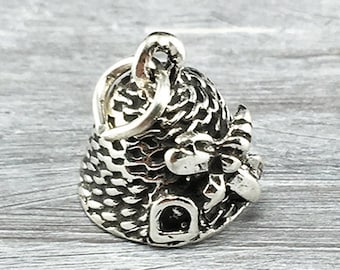 May include: A silver charm in the shape of a beehive with a small door and a bee on top. The charm is designed to be used on a bracelet or necklace.