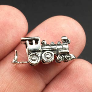 May include: Silver charm in the shape of a toy train with a black and silver finish. The train has a caboose, a locomotive, and several cars.