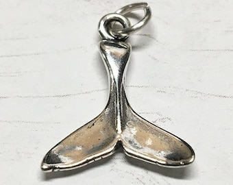 Può includere: Un ciondolo a forma di coda di balena in argento. La coda è dettagliata e ha un anello nella parte superiore per attaccarlo a una catena o un braccialetto.