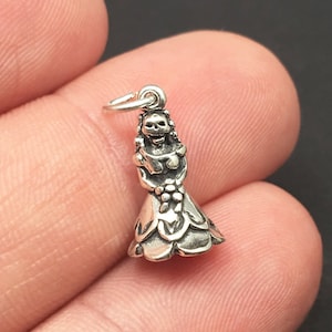 Puede incluir: Encanto de plata con una figura esquelética en un vestido, sosteniendo un ramo de flores. El encanto es un diseño tradicional del Día de Muertos.