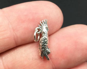 May include: A silver charm in the shape of a cockatoo bird. The charm is detailed and has a textured surface.