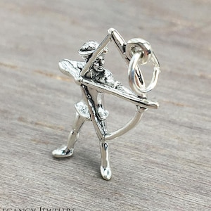 May include: Silver charm of a person holding a bow and arrow. The charm has a loop for attaching to a bracelet or necklace.
