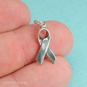 May include: Silver charm in the shape of a ribbon. The ribbon is a symbol of awareness and support for various causes.