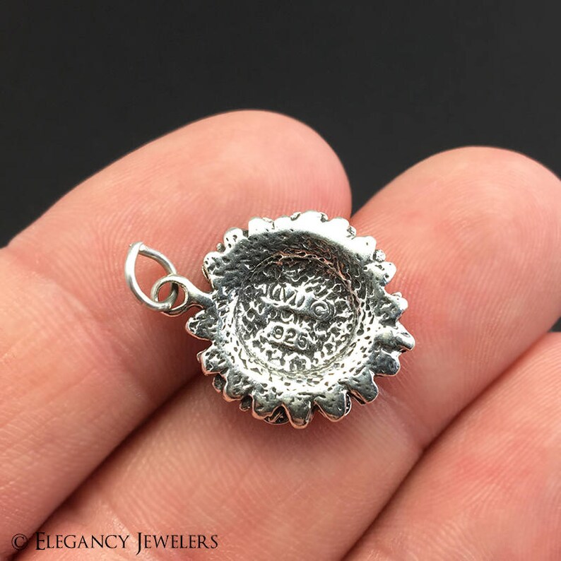 May include: Silver charm in the shape of a sunflower with a detailed design. The back of the charm has the inscription "925" indicating it is made of sterling silver.