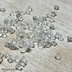 May include: A large quantity of clear plastic earring backs scattered on a light wood surface.