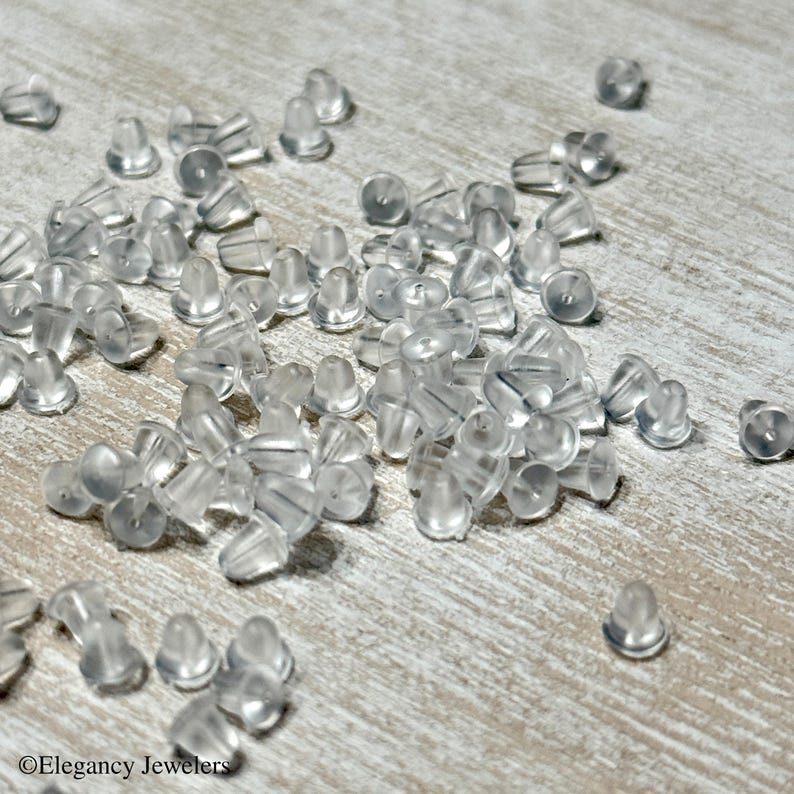 May include: A large quantity of clear plastic earring backs scattered on a light wood surface.