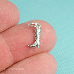 Puede incluir: Un pequeño dije de bota de vaquero plateada con intrincados detalles de volutas. El dije tiene un lazo en la parte superior para sujetarlo a un collar o pulsera. La bota mide aproximadamente 2 cm de altura, mostrando un diseño occidental clásico.
