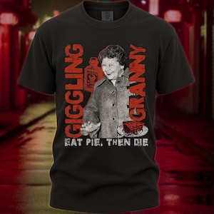 May include: Black t-shirt with a vintage-style graphic. The graphic features a smiling woman, a pie, and a poison bottle, with the words "GIGGLING GRANNY" and "EAT PIE, THEN DIE" in red lettering. The shirt has a crew neck and short sleeves.