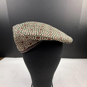 May include: A flat cap featuring a repeating geometric pattern of squares in shades of cream, dark brown, and black. The hat has a structured crown and a short, stiff brim, showcasing a woven texture throughout the fabric of the cap's exterior.