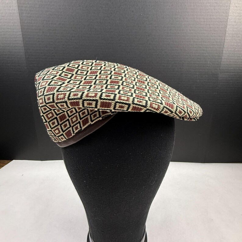 May include: A flat cap featuring a repeating geometric pattern of squares in shades of cream, dark brown, and black. The hat has a structured crown and a short, stiff brim, showcasing a woven texture throughout the fabric of the cap's exterior.