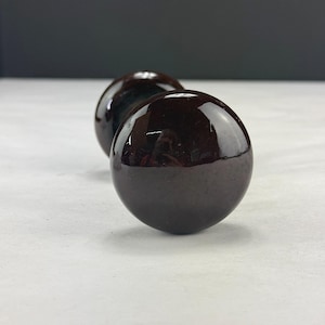 May include: Two dark brown, glossy, spherical objects are positioned on a white surface. The spheres have a smooth, reflective surface, with a slight gradient in color. The background is a dark gray.