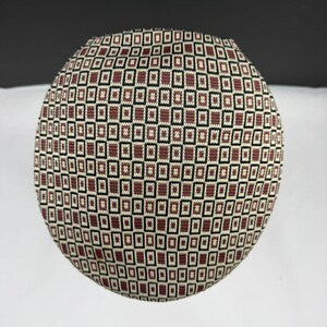 May include: A circular, flat-topped hat featuring a repeating geometric pattern of small, brown, black, and cream-coloured rectangles. The knit fabric displays a structured, grid-like design that covers the entire surface of the rounded headwear.