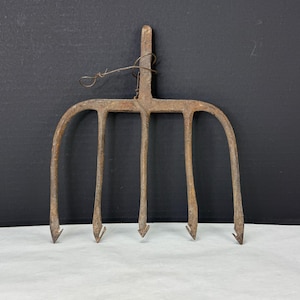 May include: A vintage, rusty metal pitchfork with five tines. The pitchfork has a long handle and is bound with wire. The tines are curved and pointed. The tool is likely used for gardening or farming.