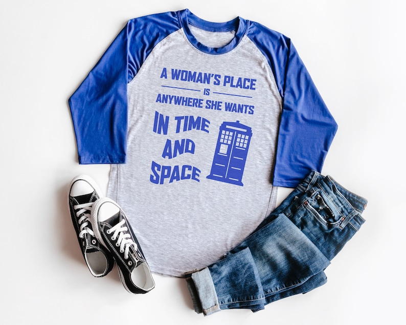 May include: A gray and blue baseball tee shirt with the text "A woman's place is anywhere she wants in time and space" and a blue TARDIS graphic.