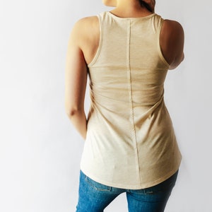 May include: A light beige sleeveless tank top with a scoop neck and a straight hemline. The tank top is made of a soft, comfortable fabric and has a relaxed fit.
