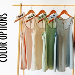 May include: Four tank tops hanging on a wooden rack. The tank tops are in the colors blush, oatmeal, sea glass, and steel.