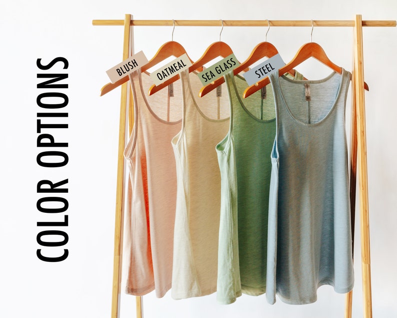 May include: Four tank tops hanging on a wooden rack. The tank tops are in the colors blush, oatmeal, sea glass, and steel.