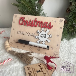 Puede incluir: Un letrero de cuenta atrás de Navidad de madera con un copo de nieve blanco y un marcador negro. El letrero dice "Christmas Countdown 128".