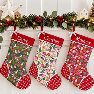 May include: Three Christmas stockings with red cuffs featuring the names Daddy, Charles, and Mummy in white embroidery. Each stocking has a patterned body with colourful geometric shapes, trees, and birds, finished with a red and white polka dot toe.