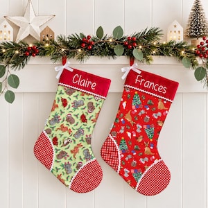May include: Two Christmas stockings with white ribbon bows at the top. The left stocking is light green with koala and animal prints, labelled Claire. The right stocking is red with kangaroo and tree prints, labelled Frances. Both have red polka-dot heels and toes.