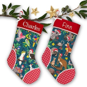 May include: Two Christmas stockings with red polka dot detailing and red tops. One stocking has the name "Charles" and the other has "Finn". Both feature a teal background with Australian animals and birds wearing Santa hats.