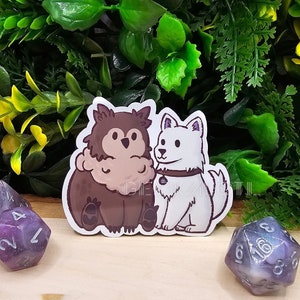 May include: A sticker depicting two cartoon dogs, one brown and one white, side by side. The brown dog has fluffy fur, and the white dog wears a collar. Purple and white dice are scattered around the sticker on a wooden surface.