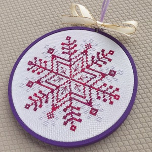 May include: A purple and white snowflake cross-stitch ornament with a white ribbon.