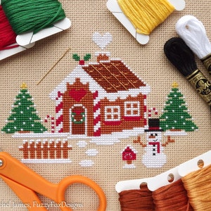 May include: Cross stitch pattern of a gingerbread house with candy canes, a snowman, and two Christmas trees. The pattern is on Aida cloth and includes DMC floss in various colors.