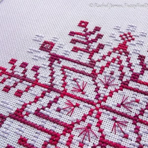 May include: Close-up of a cross-stitch pattern with a geometric design in shades of pink and purple on white Aida cloth.