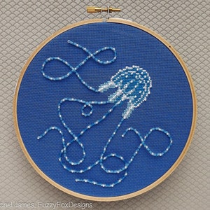 May include: A blue and white cross-stitch embroidery of a jellyfish with long, flowing tentacles. The embroidery is framed in a wooden hoop.