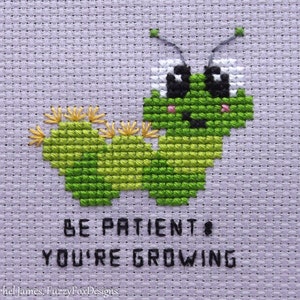 May include: Cross stitch pattern featuring a green cartoon caterpillar with a smiling face and the text "Be patient, you're growing".