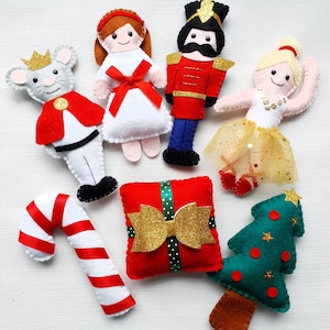 May include: A set of felt Christmas decorations featuring a nutcracker, a ballerina, a mouse, a candy cane, a present, and a Christmas tree. The decorations are all handmade and feature intricate details.