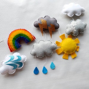 May include: A colorful felt mobile with a rainbow, clouds, a sun, lightning bolts, and raindrops. The mobile is made of felt and is perfect for a nursery or child's room.