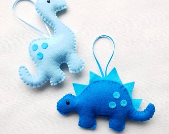 May include: Two felt dinosaur ornaments, one blue and one light blue, with hanging loops. The blue dinosaur has spikes on its back and the light blue dinosaur has a long neck.